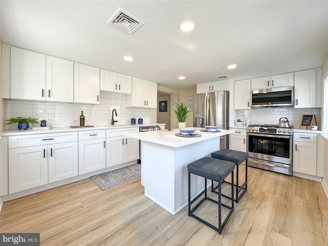 kitchen with stainless steel appliances, white cabinetry, visible vents, and light wood finished floors