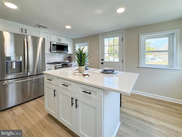 kitchen with tasteful backsplash, visible vents, light wood-style flooring, white cabinets, and stainless steel appliances