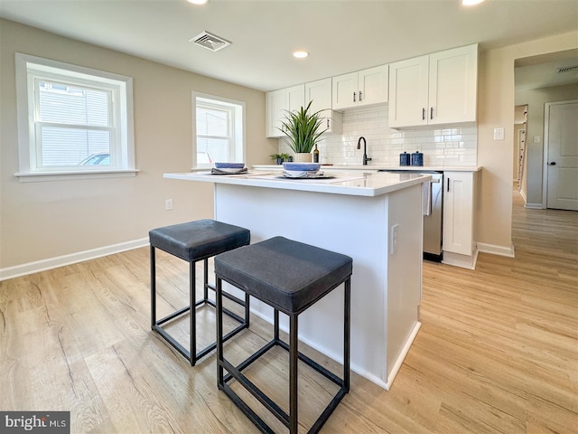 kitchen featuring visible vents, a kitchen breakfast bar, tasteful backsplash, a center island, and white cabinets