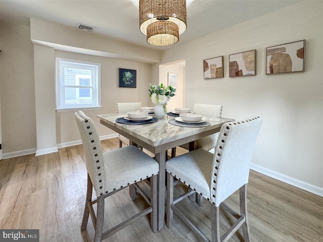 dining area with light wood-type flooring, visible vents, baseboards, and a notable chandelier