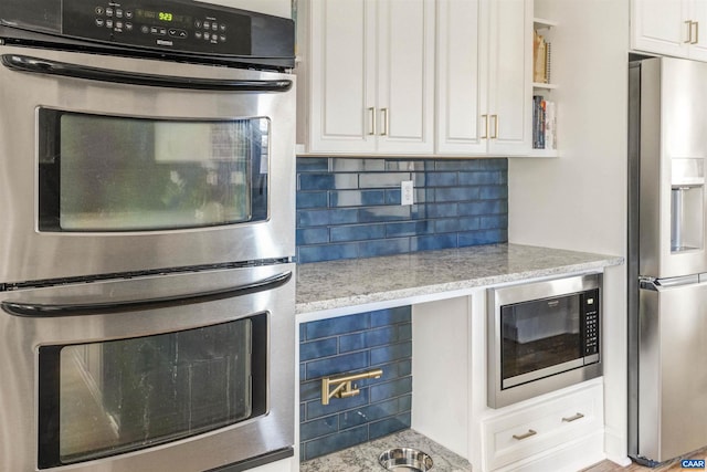 kitchen with decorative backsplash, light stone counters, white cabinetry, and stainless steel appliances