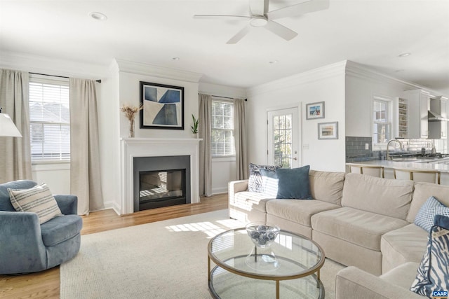 living room featuring plenty of natural light, a glass covered fireplace, ornamental molding, and light wood finished floors