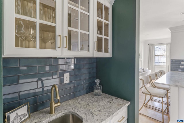 kitchen with light stone countertops, a sink, glass insert cabinets, white cabinetry, and backsplash