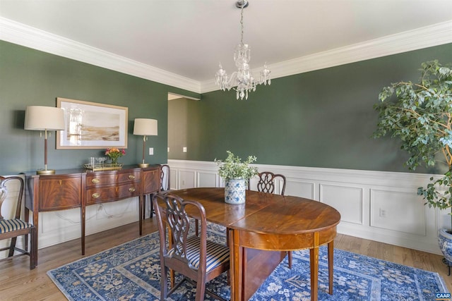 dining room featuring an inviting chandelier, wood finished floors, wainscoting, and ornamental molding