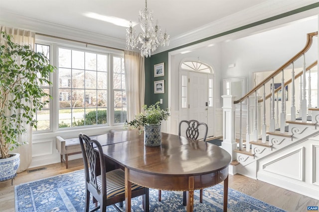 dining space featuring stairway, visible vents, an inviting chandelier, ornamental molding, and a decorative wall