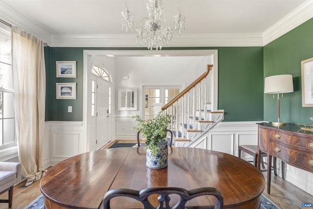 dining area with a wainscoted wall, wood finished floors, stairway, an inviting chandelier, and crown molding