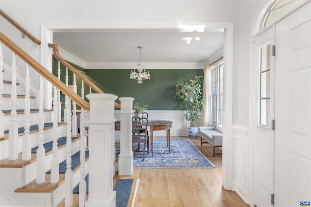 entryway with stairway, a notable chandelier, crown molding, and light wood finished floors