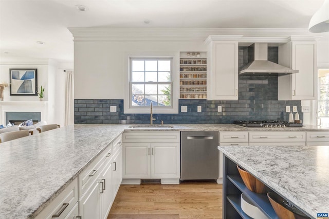 kitchen featuring appliances with stainless steel finishes, a fireplace, white cabinets, wall chimney exhaust hood, and a sink