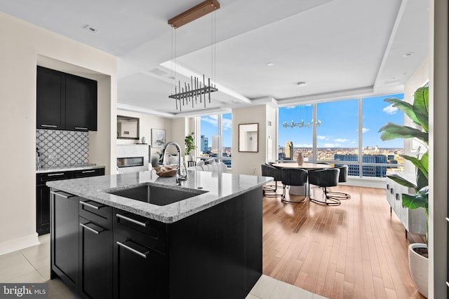 kitchen featuring open floor plan, an island with sink, decorative backsplash, dark cabinetry, and a sink