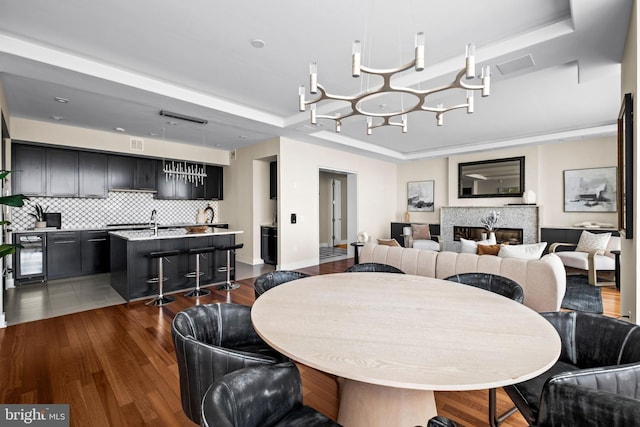 dining room with a raised ceiling, dark wood-type flooring, beverage cooler, and a high end fireplace