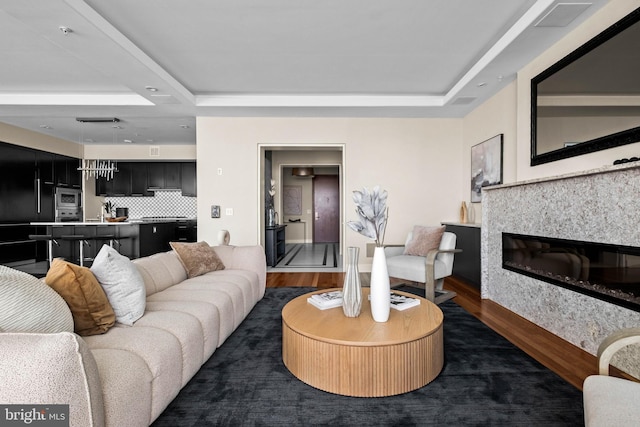 living area featuring dark wood finished floors, a raised ceiling, and a glass covered fireplace