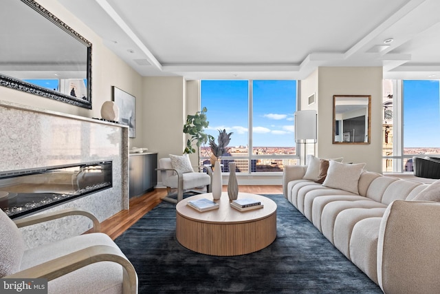 living room featuring wood finished floors, visible vents, floor to ceiling windows, a glass covered fireplace, and a raised ceiling