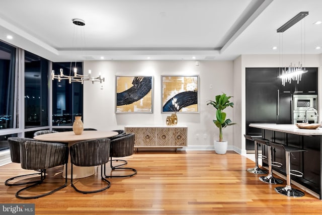 dining area with baseboards, light wood-style flooring, recessed lighting, a raised ceiling, and a notable chandelier