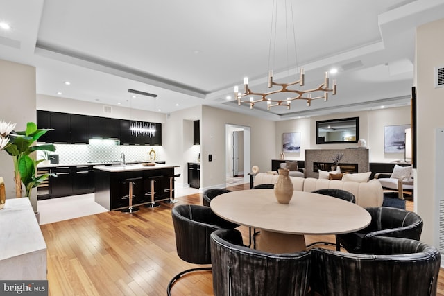 dining area featuring visible vents, light wood-style flooring, a tray ceiling, a glass covered fireplace, and recessed lighting