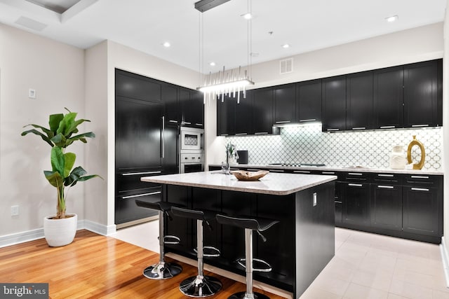 kitchen with visible vents, built in appliances, light stone counters, decorative backsplash, and dark cabinetry