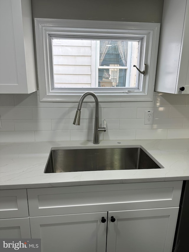 room details with white cabinetry, light stone counters, tasteful backsplash, and a sink