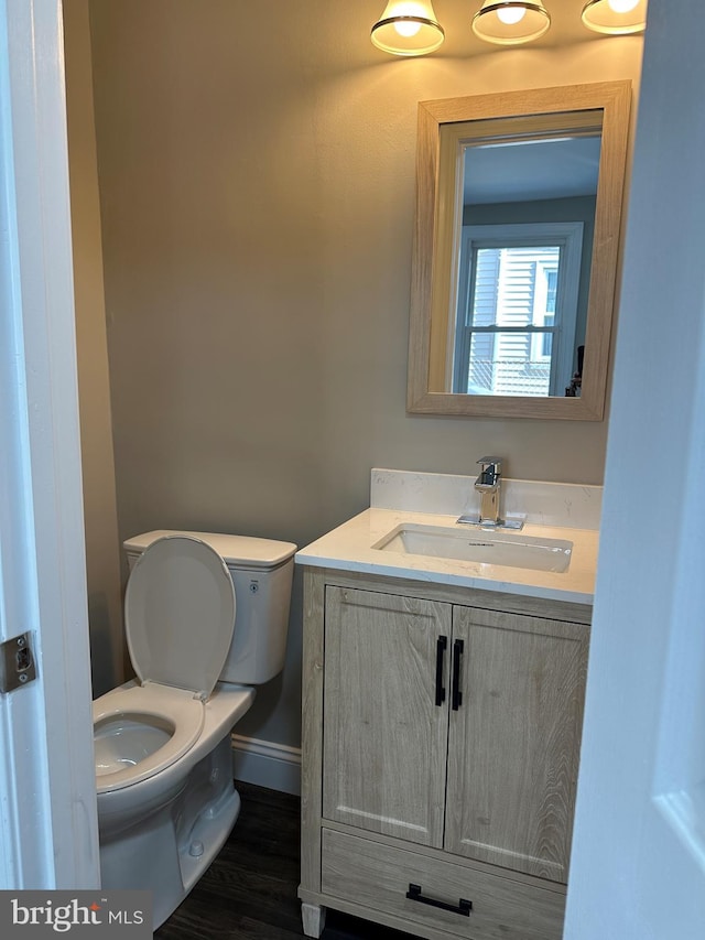 half bathroom with vanity, toilet, wood finished floors, and baseboards