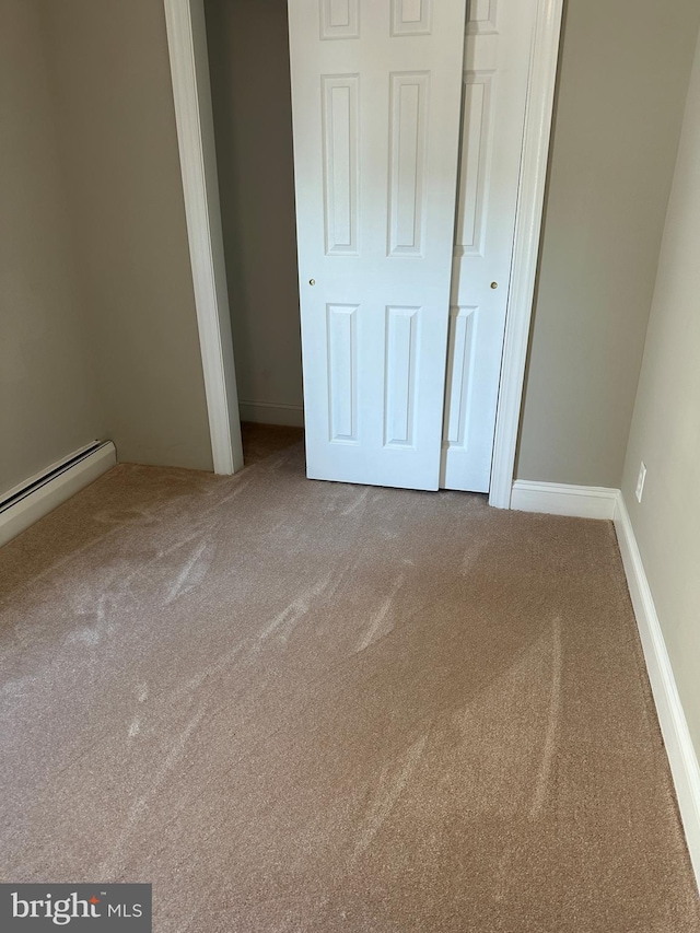 unfurnished bedroom featuring a baseboard heating unit, baseboards, and carpet floors