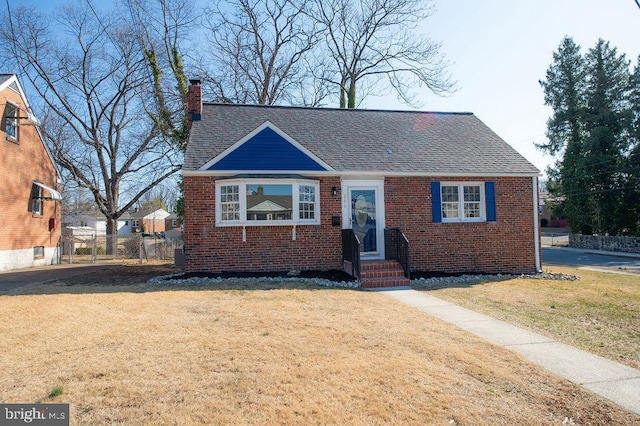 bungalow with brick siding, a chimney, a front yard, and a shingled roof