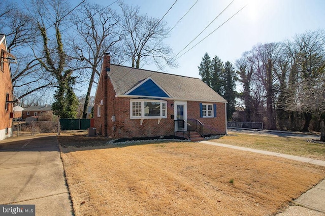 view of front of home with brick siding, a shingled roof, a front lawn, fence, and a chimney