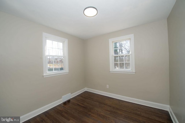 spare room featuring dark wood finished floors, visible vents, and baseboards