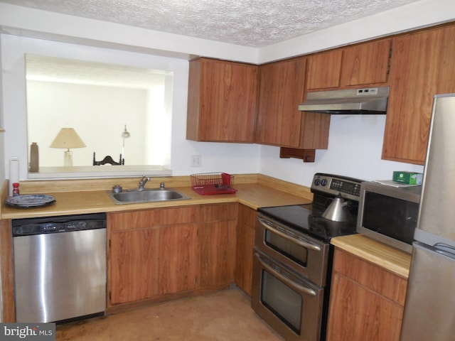 kitchen featuring a sink, light countertops, appliances with stainless steel finishes, a textured ceiling, and under cabinet range hood