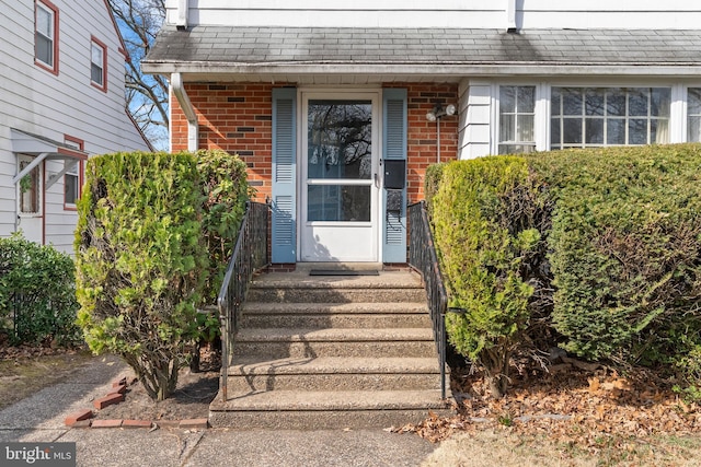 doorway to property with brick siding and roof with shingles