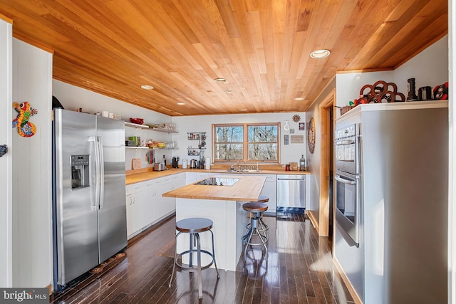 kitchen with a sink, butcher block countertops, appliances with stainless steel finishes, white cabinetry, and a kitchen breakfast bar