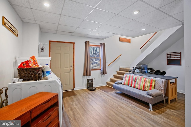 living area with stairway, a drop ceiling, baseboards, and wood finished floors