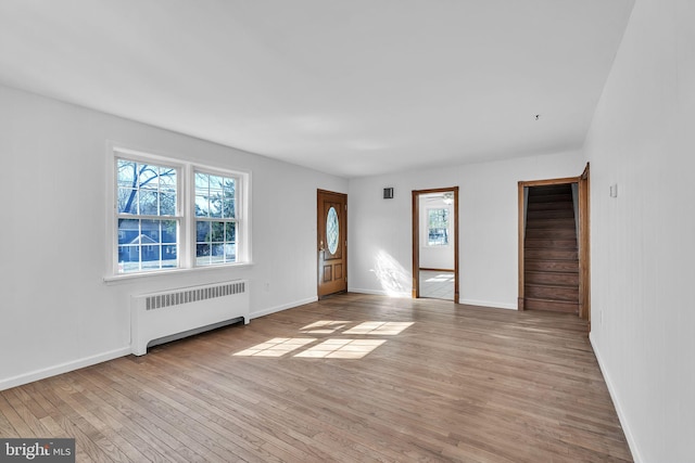 unfurnished living room with stairs, baseboards, light wood-style floors, and radiator heating unit