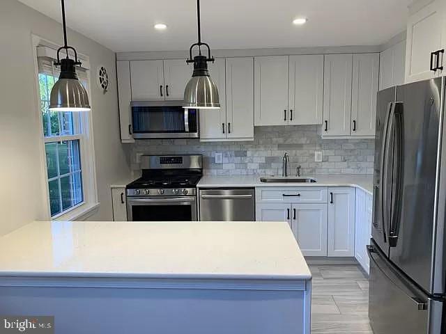 kitchen featuring a sink, white cabinetry, stainless steel appliances, light countertops, and decorative backsplash