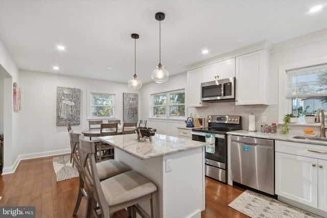 kitchen featuring dark wood-style flooring, stainless steel appliances, white cabinets, backsplash, and a center island