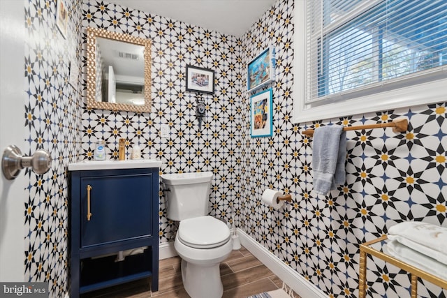 half bathroom with visible vents, toilet, wood tiled floor, baseboards, and vanity