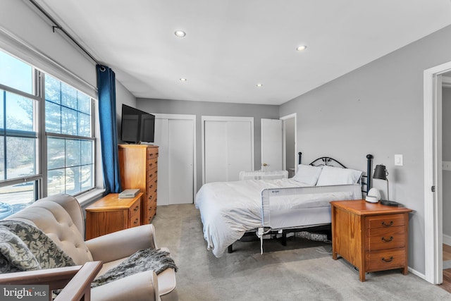 bedroom with recessed lighting, light colored carpet, baseboards, and two closets