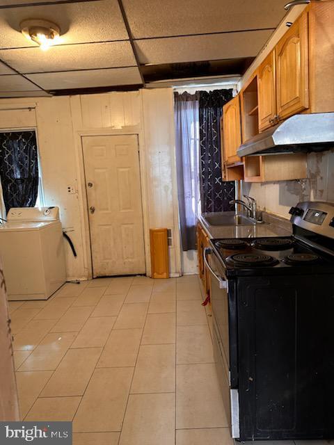 kitchen with a sink, a paneled ceiling, under cabinet range hood, range with electric stovetop, and brown cabinets