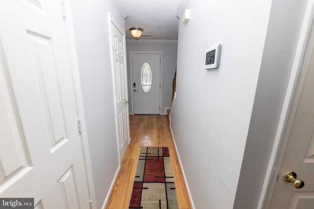 doorway to outside with light wood-type flooring, baseboards, and crown molding