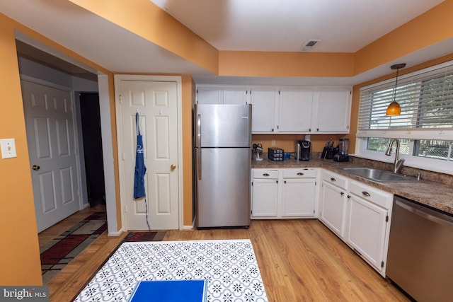 kitchen with a sink, decorative light fixtures, white cabinetry, stainless steel appliances, and light wood finished floors