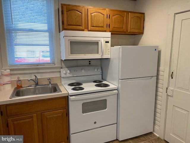 kitchen featuring white appliances, brown cabinetry, light countertops, and a sink