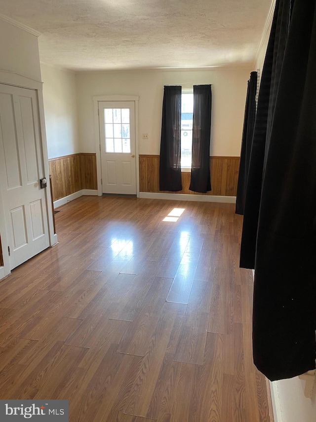 empty room featuring wooden walls, a textured ceiling, wood finished floors, and wainscoting