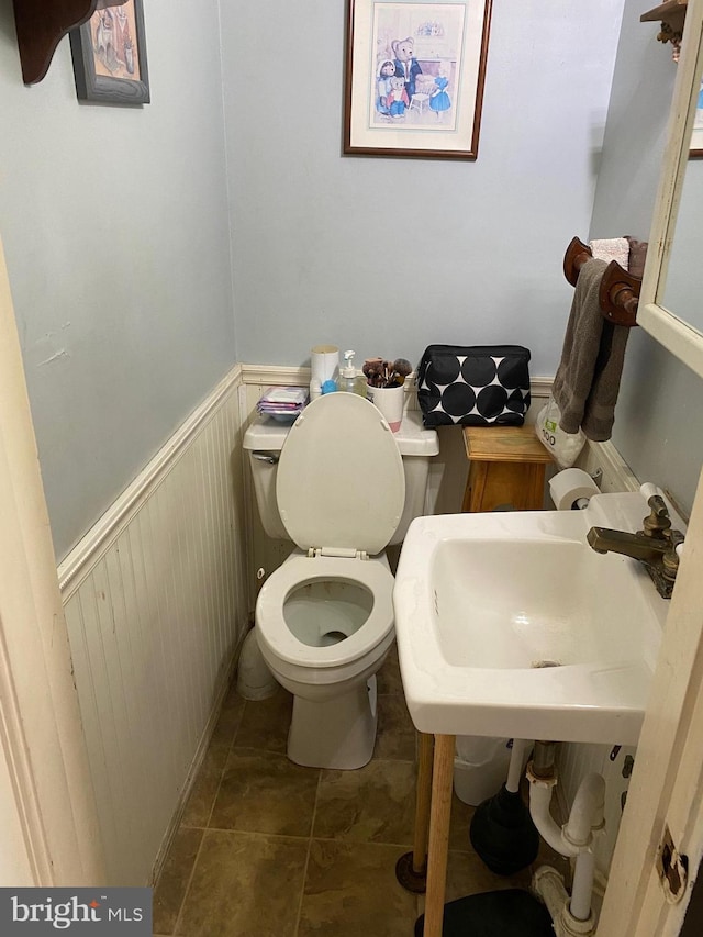 half bathroom with tile patterned floors, toilet, a wainscoted wall, and a sink