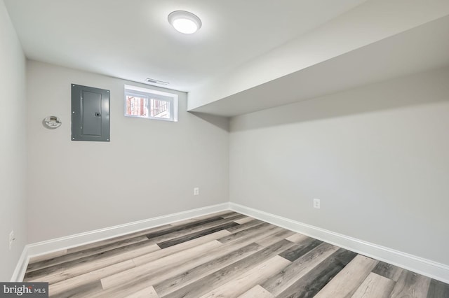 below grade area with electric panel, visible vents, baseboards, and wood finished floors