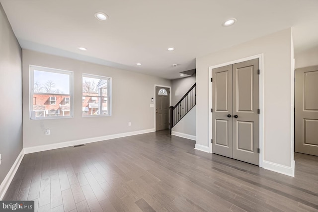 unfurnished living room with recessed lighting, stairway, baseboards, and dark wood-type flooring