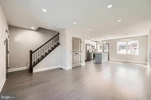 unfurnished living room with dark wood finished floors, stairway, recessed lighting, and baseboards