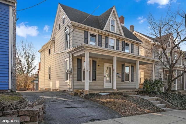 view of front of house featuring aphalt driveway, covered porch, and a shingled roof