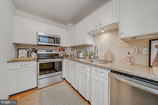 kitchen featuring a sink, stainless steel appliances, light stone counters, and white cabinets