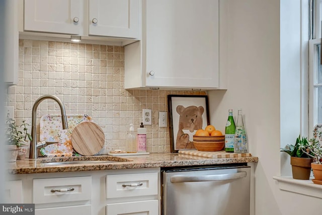 kitchen with a sink, tasteful backsplash, stainless steel dishwasher, white cabinetry, and light stone countertops