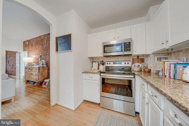 kitchen with tasteful backsplash, stainless steel appliances, arched walkways, white cabinets, and light wood finished floors