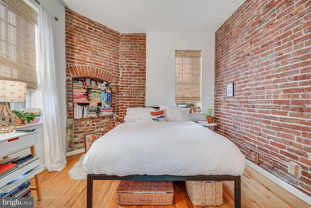 bedroom with baseboards, wood finished floors, and brick wall