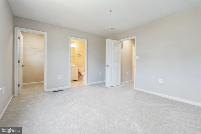 unfurnished bedroom with baseboards, a closet, a walk in closet, light colored carpet, and connected bathroom