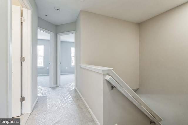 hallway featuring an upstairs landing, baseboards, and light carpet